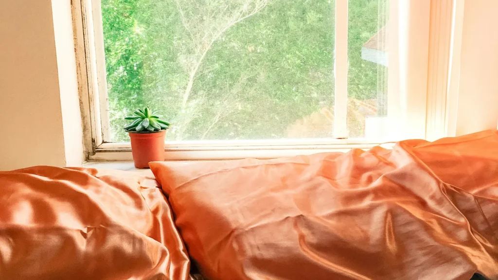 White bed linen and pillows beside a sunlit window in a calm, naturally lit bedroom